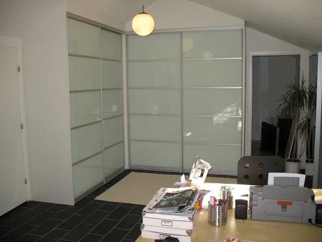 Indbygget klædeskab med skydedøre af mat glas i lyse metalrammer i et tagværelse med skråt loft
