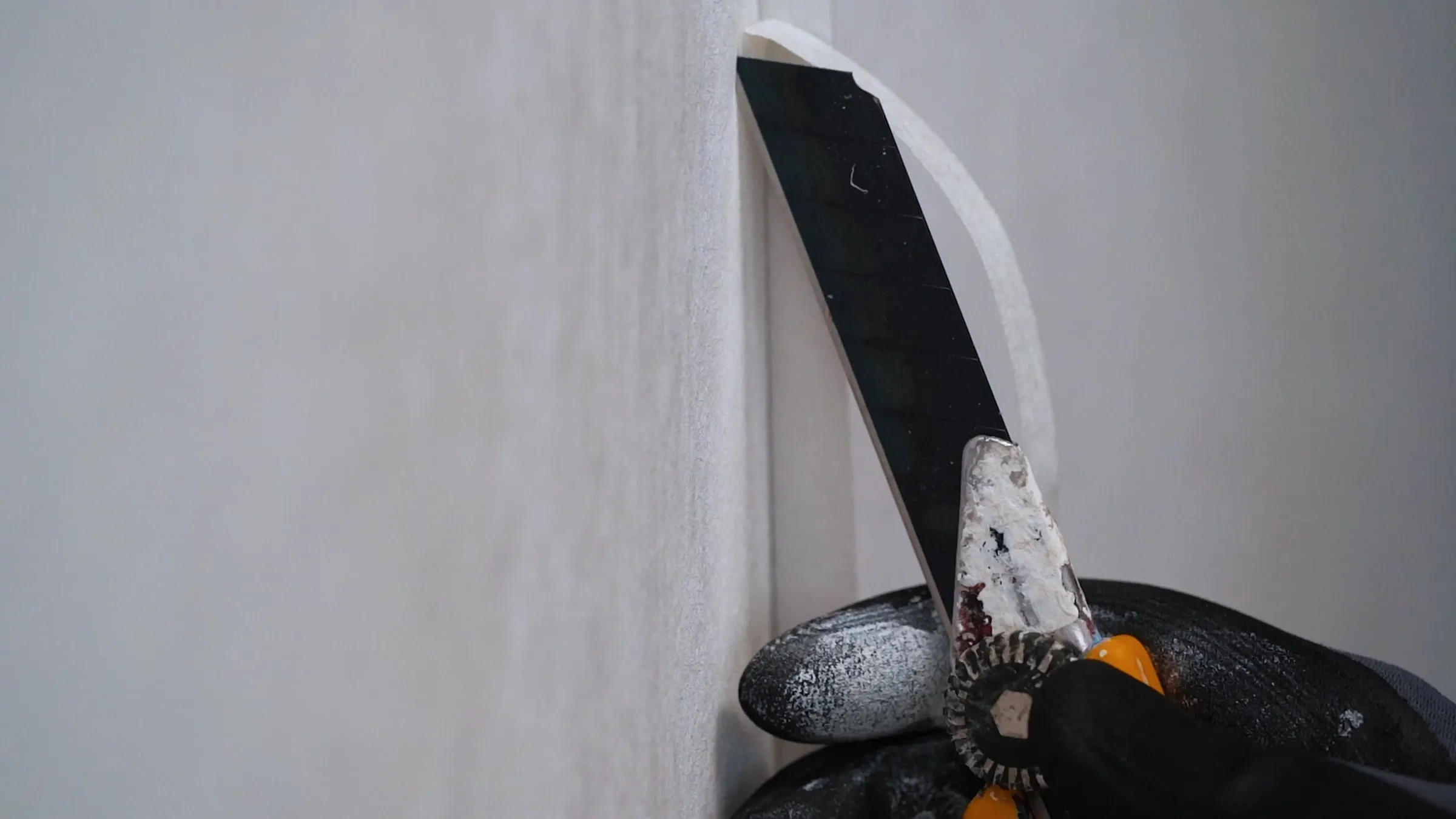 Hobbykniv og spartel skærer en hvid bane til i hjørnet af en væg