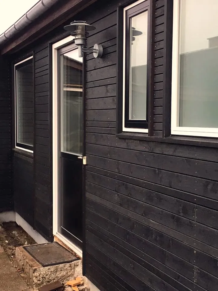 Sortmalet træbeklædning på tilbygning med hvide vindues- og dørpartier