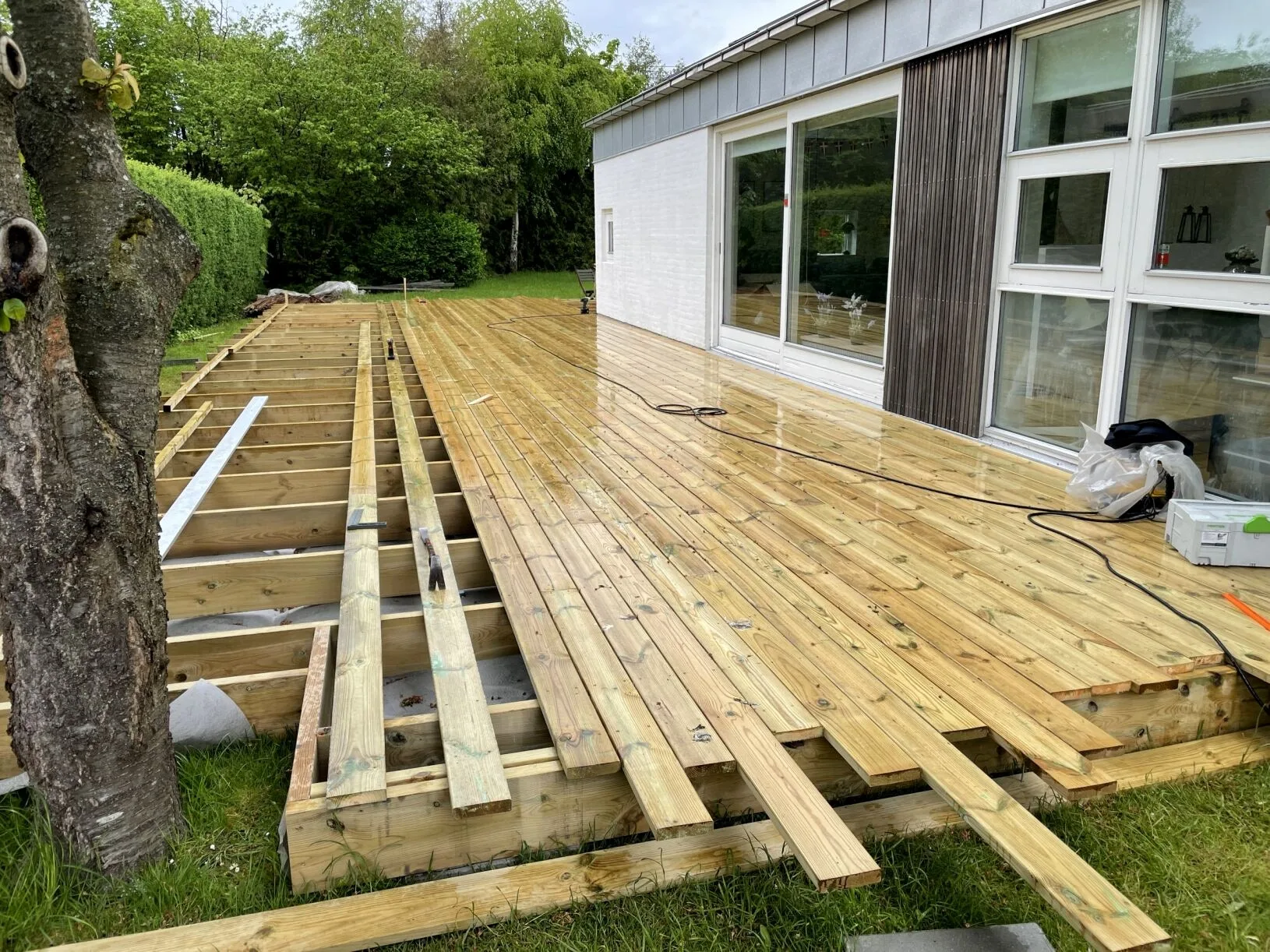 Terrassedæk under opbygning med synlige strøer foran parcelhus
